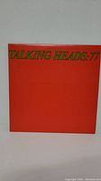 Front cover of Talking Heads: 77 album showing bright red cover with green title text.