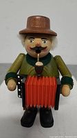 Front view of the wooden accordion player figurine with a pipe and red accordion.