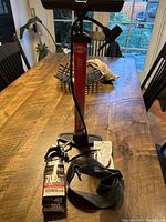 Photo displaying a black and red floor pump with pressure gauge, a 700c inner tube, and a tire patch kit on a wooden table.