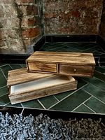 Set of two wooden storage boxes with drawers and sliding lids placed on floor tiles with exposed brick wall background.