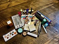 Top-down view of all makeup items and the hair curler on a wooden surface, showing variety and packaged condition.