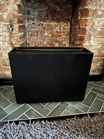 Closed view of black plastic floating shoe rack against brick wall and tile floor.