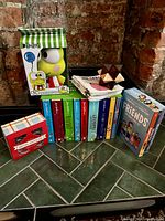 Photo showing Keroppi plush toy box, colorful children's books/DVDs, Friends DVD, metal puzzles box, wooden puzzle, and small stack of books/notebooks.