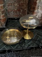 Two matching IKEA table lamps on a dark tiled surface with brass finish and clear glass domes. Both lamps have black cords and visible bulbs inside glass domes.