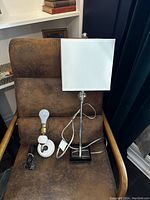 Both lamps displayed on brown chair: decorative milk glass wall sconce and desk lamp with white square shade