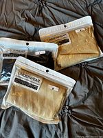 Three unopened packages of tummy control shapewear thongs, two tan and one black, with size labels visible.