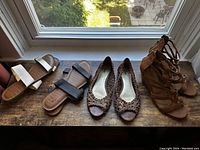 Top-down view of four pairs of women's shoes on a wooden surface by a window including flat sandals and flats.