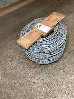 Full roll of coiled galvanized steel barbed wire with wooden securing boards on concrete floor.