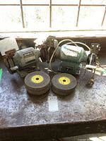 Photo showing both Delta and Hitachi bench grinders with spare grinding wheels on a workbench.