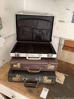Opened three briefcases stacked: silver on top, brown middle, black bottom, showing front and interior details.
