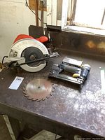 Black & Decker circular saw and Mastercraft brad nailer side by side with a spare circular saw blade on a metal surface