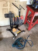 Wide shot of the larger square tire dolly, Bike Master tire dolly, new mud flaps, hand pump, and two small blue air hoses coiled on the ground.