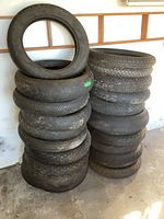 Photo shows two stacks of motorcycle tires with various tread patterns and sizes, some worn slick racing types and others street tires.