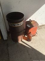 Photo showing the three items: the metal hazardous waste step lid can, the rusty Dunlop trash can, and the amber glass bottle with a small chip.