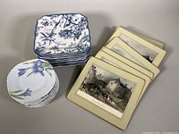 Top view of all plates including square blue and white plates with birds and floral motifs, round plates with blue bellflower designs, and some decorative prints beneath.