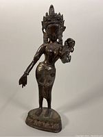 Front view of the brass Hindu goddess sculpture showing detailed carving, crown, and outstretched arms on pedestal base.