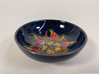 Angled view of small shallow pottery bowl with colorful floral pattern on dark blue background.