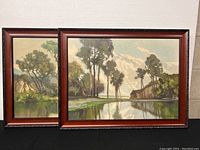 Two framed landscape prints showing calm water with trees and hills under partly cloudy sky, frames have reddish-brown wood tone and minor wear.
