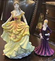Two Royal Doulton porcelain figurines displayed on a table, showing size difference and detailing.