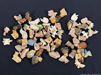 Top-down view of 30+ miniature porcelain figurines scattered on a surface, showing variety in shapes and colors highlighting wear like some chips