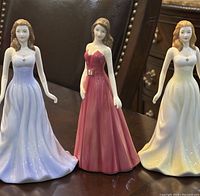 Front view of all three Royal Doulton figurines together on a table, showing their dresses and details.