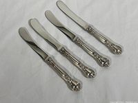 Four Birks butter spreaders laid out in a row showing full length and handle design.