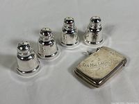 Photo showing two pairs of sterling silver salt and pepper shakers alongside the monogrammed match holder with striker.