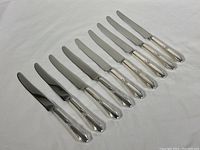 Nine dinner knives with sterling silver handles and stainless steel blades laid out in a row, showing overall good condition and consistent handle design.