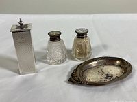 Photo showing the set: rectangular silver shaker, two crystal salt and pepper shakers with silver lids, and oval silver nut dish with tarnish and dents