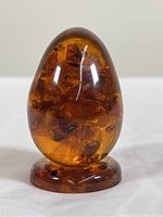 Photo of amber egg sculpture on its stand under normal light showing the polished amber with natural inclusions inside.