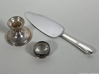Overall view of all three items in the lot placed together, showing cake cutter, napkin ring, and candleholder.