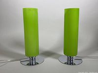 Pair of green cylindrical table lamps with chrome round bases against a white background. Lamps are off, showing green shade color and minor wear at top.