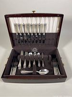 Open wooden chest displaying various types of vintage silver-tone flatware including forks and spoons arranged upright in the top and bottom fits.