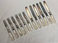 Full set of 6 knives and 6 forks laid out with mother of pearl handles and tarnished engraved blades/tines
