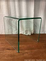 View of the thick curved glass side table showing U-shaped design and slightly green edges.