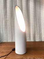 Front view of lamp illuminated, power cord and inline switch visible on table surface.