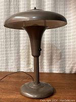 Front view of the Art Deco era aluminum table lamp with adjustable shade, showing the twist switch and weighted base.