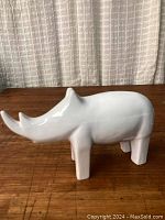 Side view of white ceramic rhino sculpture showing smooth low gloss finish and two prominent horns.