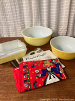 Overview of all items in the lot including tea towels, two yellow bowls, and covered baking dish on wood surface.