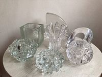 Full set of seven vintage glass art pieces placed on a round white table displaying varied textures including geometrically faceted clear glass, bark texture, and sculptural shapes.