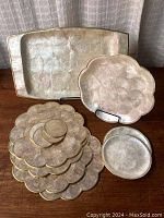 Collection of Capiz shell trays, serving dishes, and coasters arranged on a wooden surface showing pearly finishes and gold trim on some edges.
