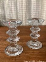 Pair of textured glass icicle-effect candlesticks shown side by side on wooden surface against fabric background