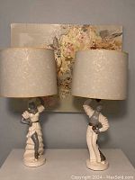Pair of unlit chalkware dancer lamps with shades in front of wall art