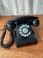 Front view of black retro rotary landline telephone on wooden surface with white curtain background.