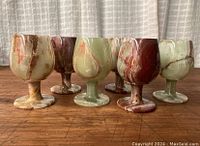 All six vintage alabaster onyx goblets displayed on a wooden surface, showing their variegated marbled colors and striated natural patterns.