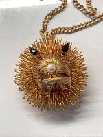 Close-up photo of goldtone vintage lion pendant with rhinestone eyes, faux pearl nose, and detailed wire mane on curb link chain.