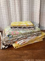 Stack of various folded vintage sheet sets and pillowcases showing floral, yellow, and brown patterns.