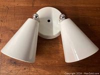 Front view of the lamp showing two white conical shades attached to round base with chrome ball joints.