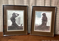 Pair of framed mermaid optical illusion art pieces shown side by side, visible dark brown mats and silver reflective artwork surfaces.