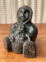Front angle of dark soapstone Inuit parent and child sculpture showing seated adult figure holding child on lap, detailed fur texture and hooded parkas.